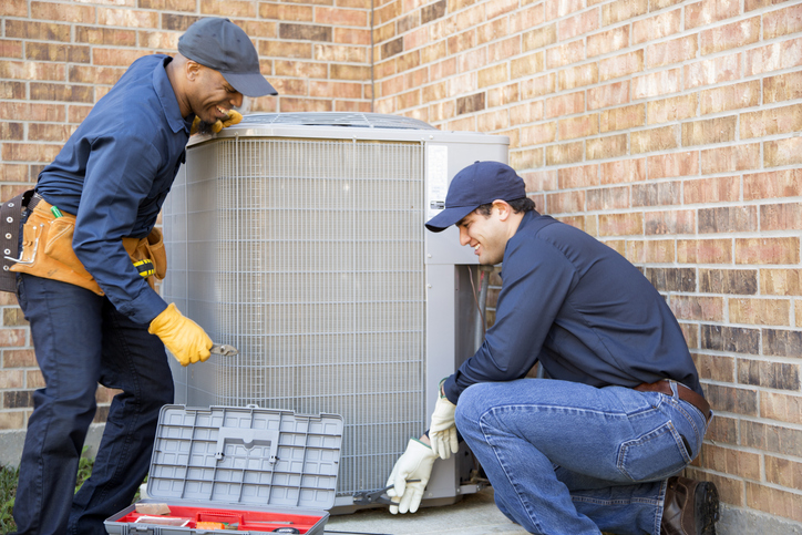 Two HVAC techs work to install an AC unit while smiling